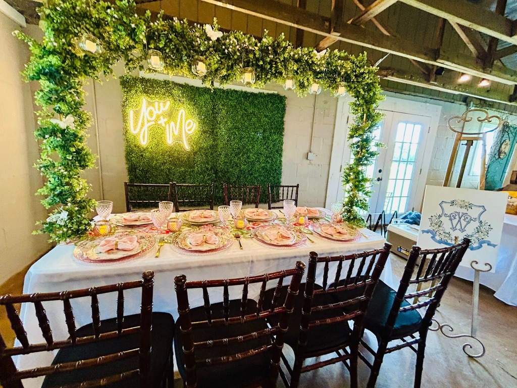 Long elegant table setting with a You + Me neon sign and boxwood backdrop