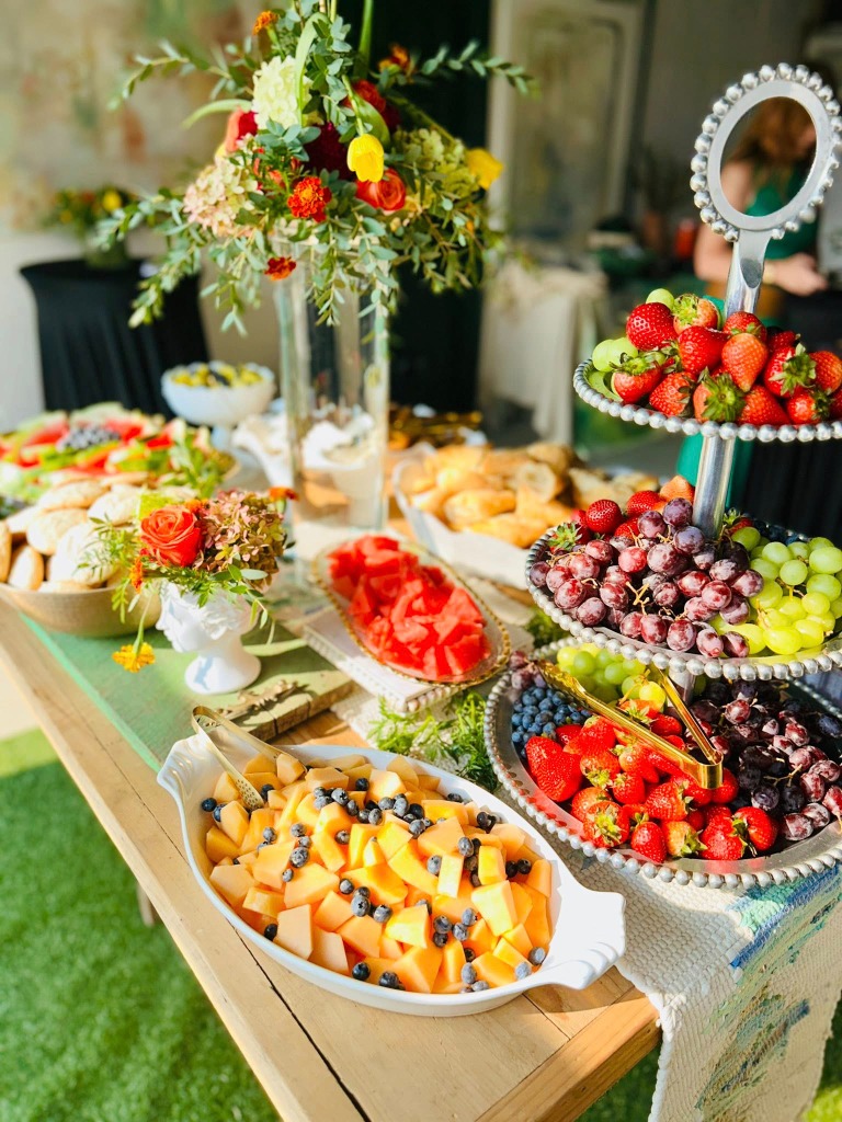 A beautiful catering display with fruit skewers, watermelon, and floral arrangements