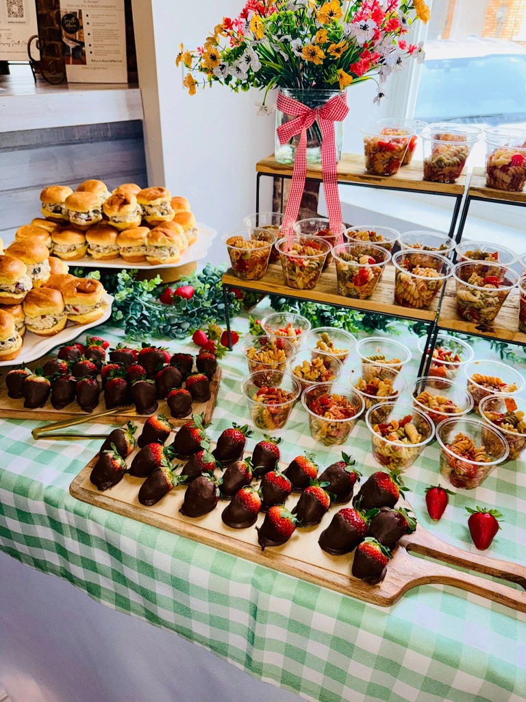 A lovely celebration setup with sandwiches, pasta salad cups, and chocolate covered strawberries