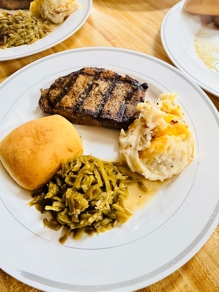 Steak, mashed potatoes, green beans, and a roll on a plate