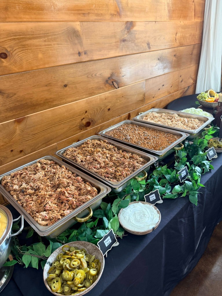 Buffet line with chafing dishes of pulled pork, baked beans, and pulled chicken