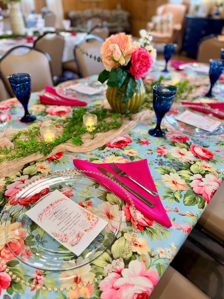 A beautifully decorated table with a floral tablecloth, pink napkins, and custom menus