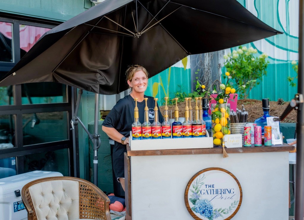 A smiling staff member at an outdoor event setup with Torani syrups and fresh lemons
