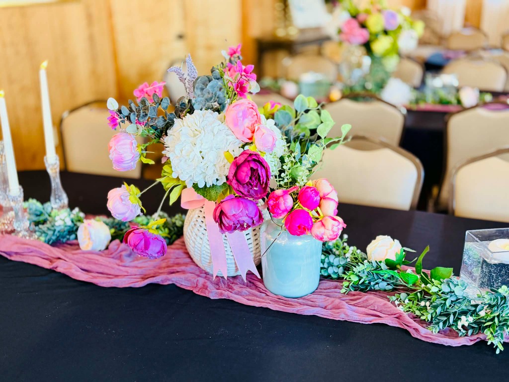 Floral centerpiece with pink peonies, roses, and greenery on dark table linen