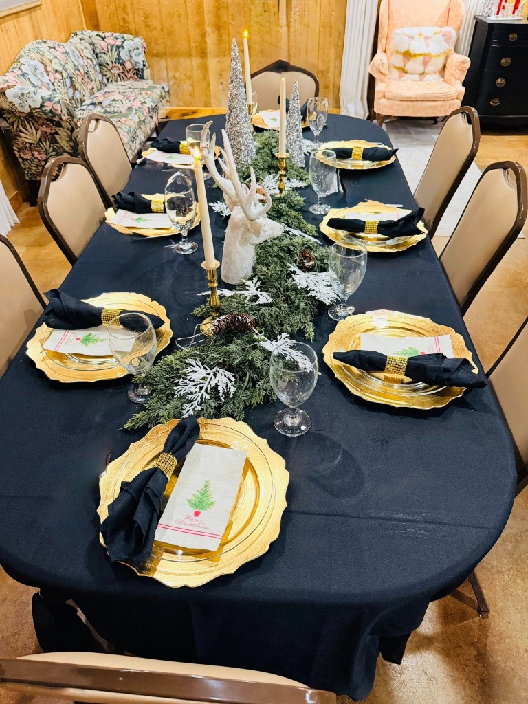 An elegant table setting with a dark tablecloth, gold chargers, and festive winter decor